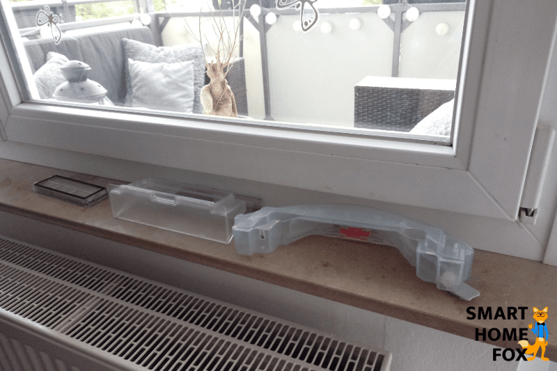 Dust bin of a robot vacuum cleaner is dried on the windowsill after washing.